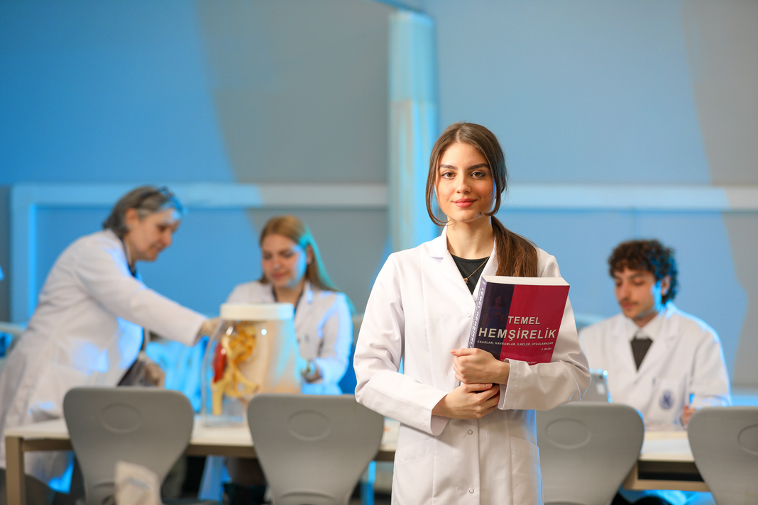 student in a white lab coat holding a medical textbook in a classroom, with other students and an anatomical model in the background. student in a white lab coat holding a medical textbook in a classroom, with other students and an anatomical model in the background.