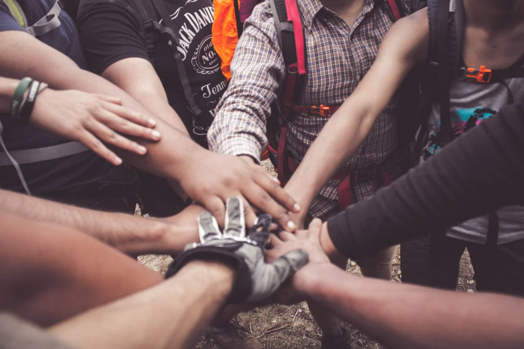 A group of people stacking their hands together in a circle, symbolizing teamwork, unity, cooperation, and mutual support.
