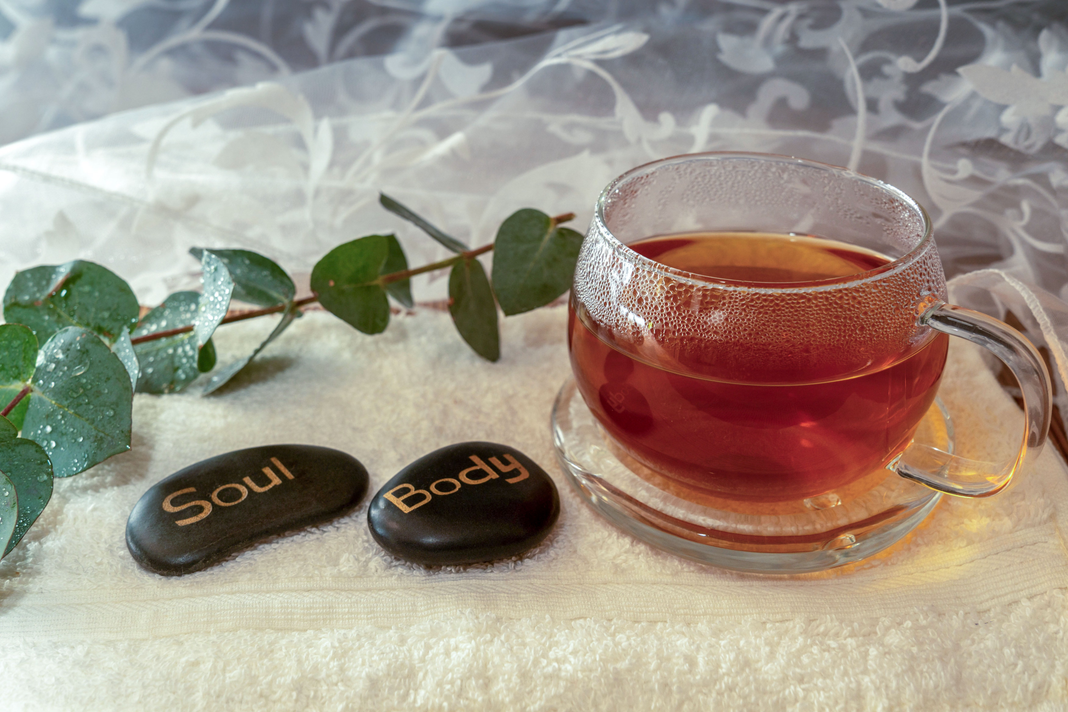 A glass cup of reddish herbal tea on a white towel beside green leaves A glass cup of reddish herbal tea on a white towel beside green leaves