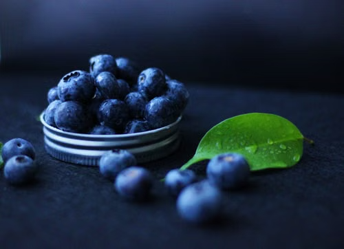 Fresh blueberries in a small bowl with a green leaf.