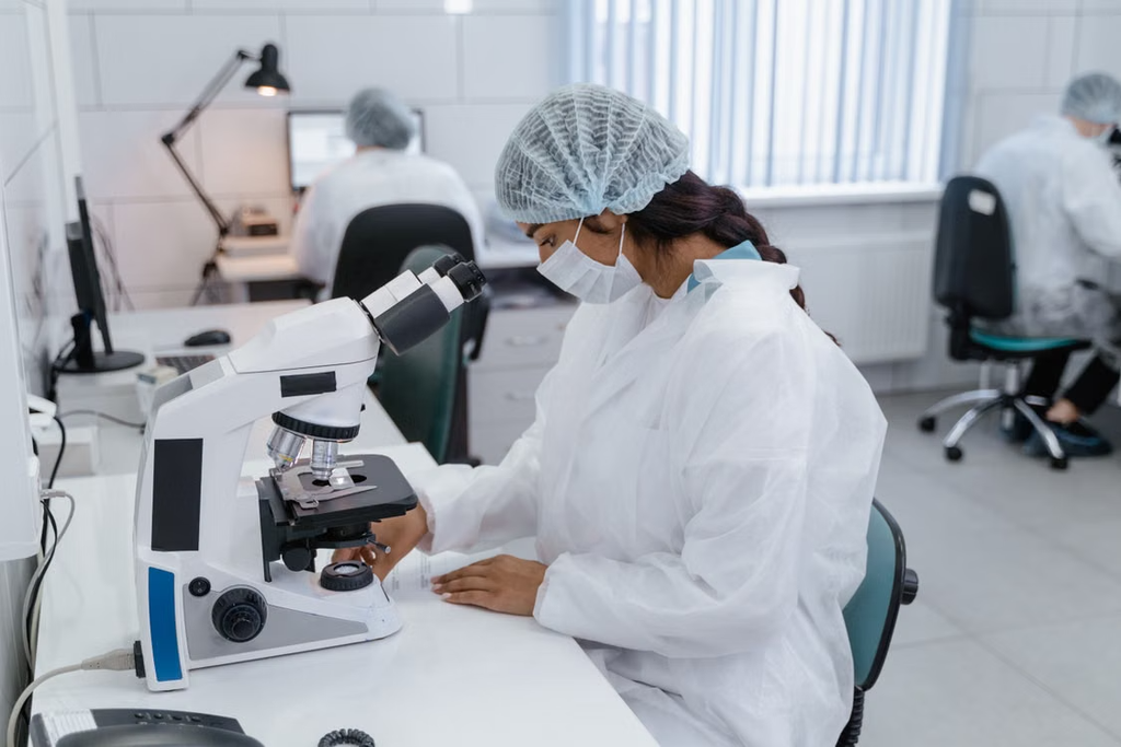Female laboratory scientist examining a sample under a microscope in medical research laboratory.
